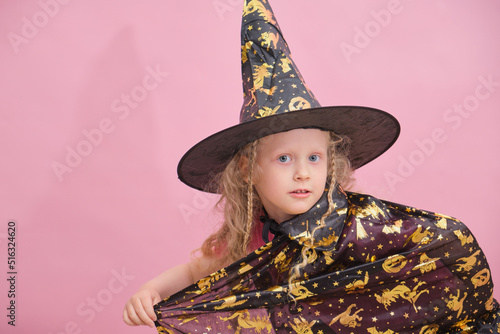 cute cheerful girl 6 years old in a witch costume on a pink background