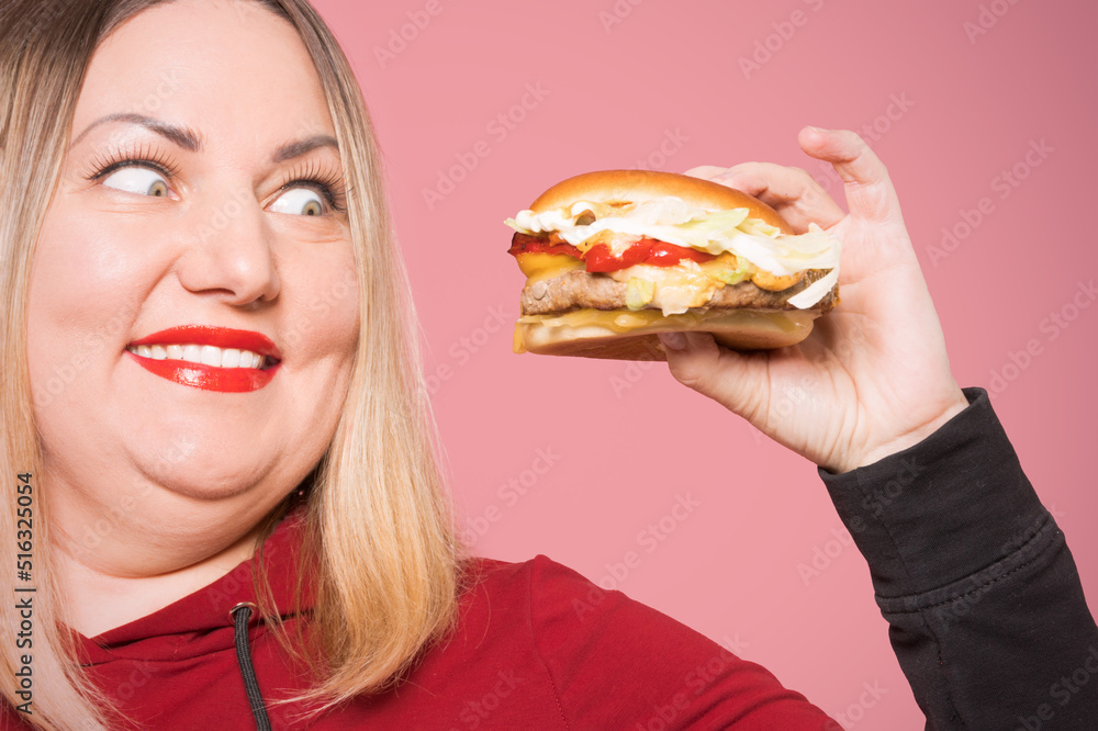 Body positive Cheerful woman with appetite looks at a delicious burger .