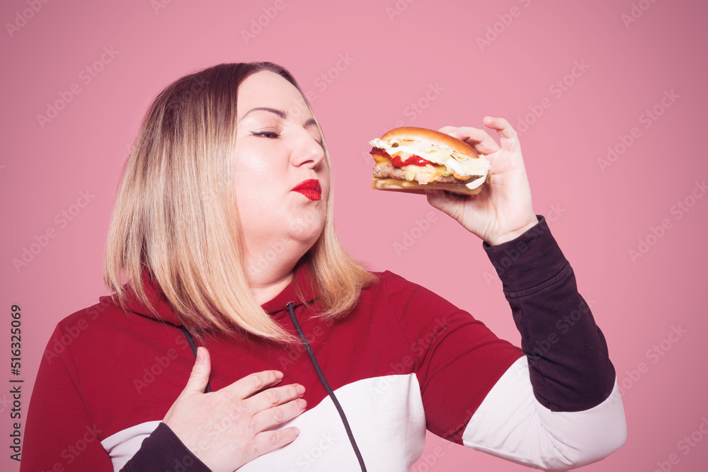 Cheerful woman with appetite looks at a delicious burger. . Unhealthy food.