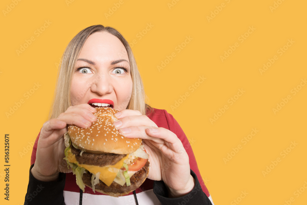 A hungry woman is biting a big tasty burger . Binge eating A hungry woman is biting a big tasty burger . Binge eating
