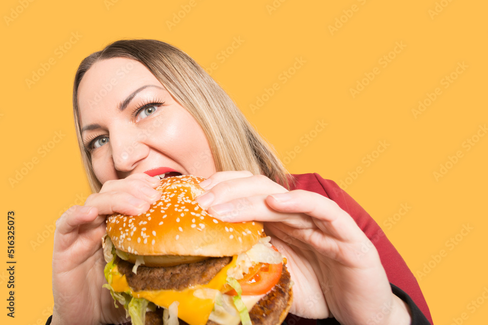 A hungry woman is biting a big tasty burger . Unhealthy food.