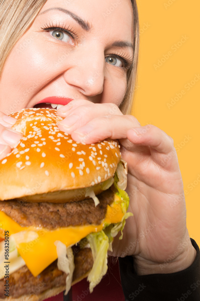 A hungry woman is biting a big tasty burger . Binge eating A hungry woman is biting a big tasty burger . Binge eating