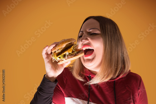 A hungry woman is biting a big tasty burger . Unhealthy food. © watman