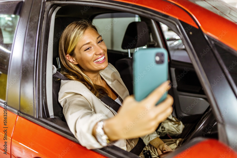 Smiling young woman taking selfie picture with smart phone camera outdoors in car. Shot of a young woman taking a selfie while sitting in her car Smiling young woman taking selfie picture with smart phone camera outdoors in car. Shot of a young woman taking a selfie while sitting in her car
