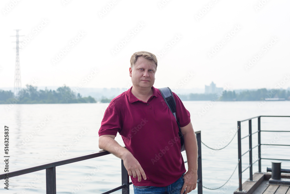 A blond man model appearance on the beach with a backpack on his shoulder.