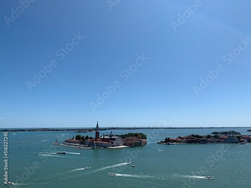 Boats at Venetian lagoon entering and leaving Venice town. Island with Church of San Giorgio Maggiore in the background. View from St. Mark's Campanile tower. Emerald blue water. Venice, Italy