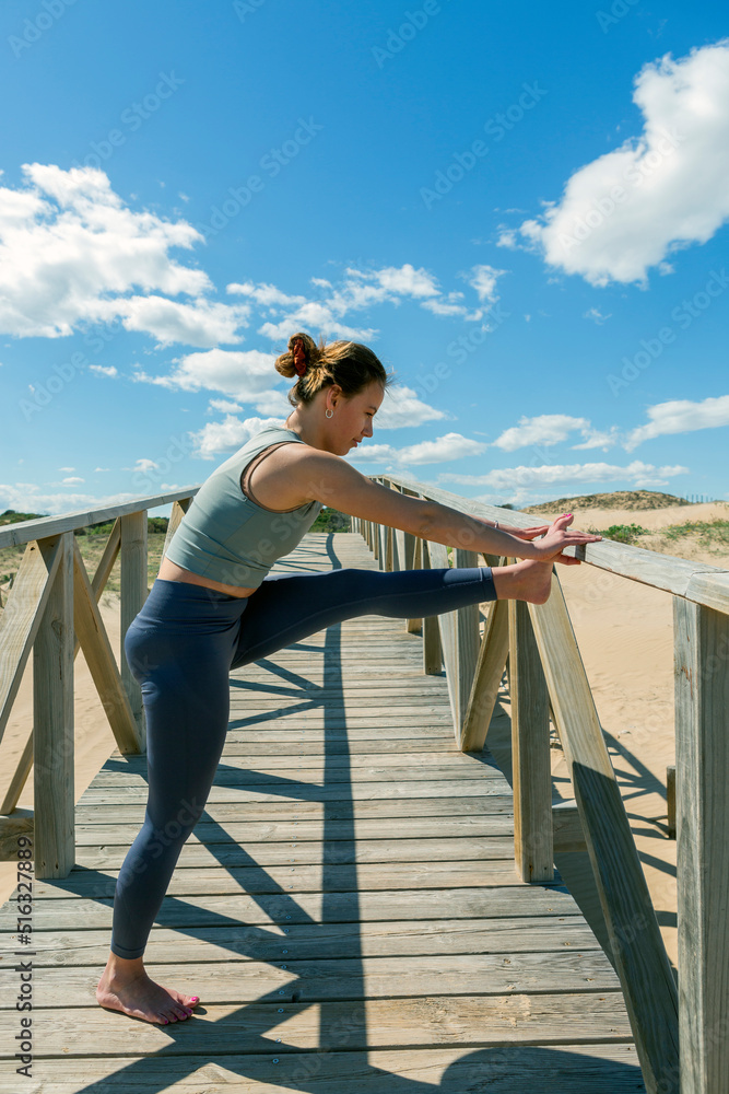 young woman performing pilates-yoga on a wooden walkway next to the beach young woman performing pilates-yoga on a wooden walkway next to the beach