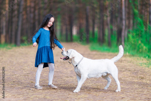 Cute little girl walks the dog in the park. White labrador.