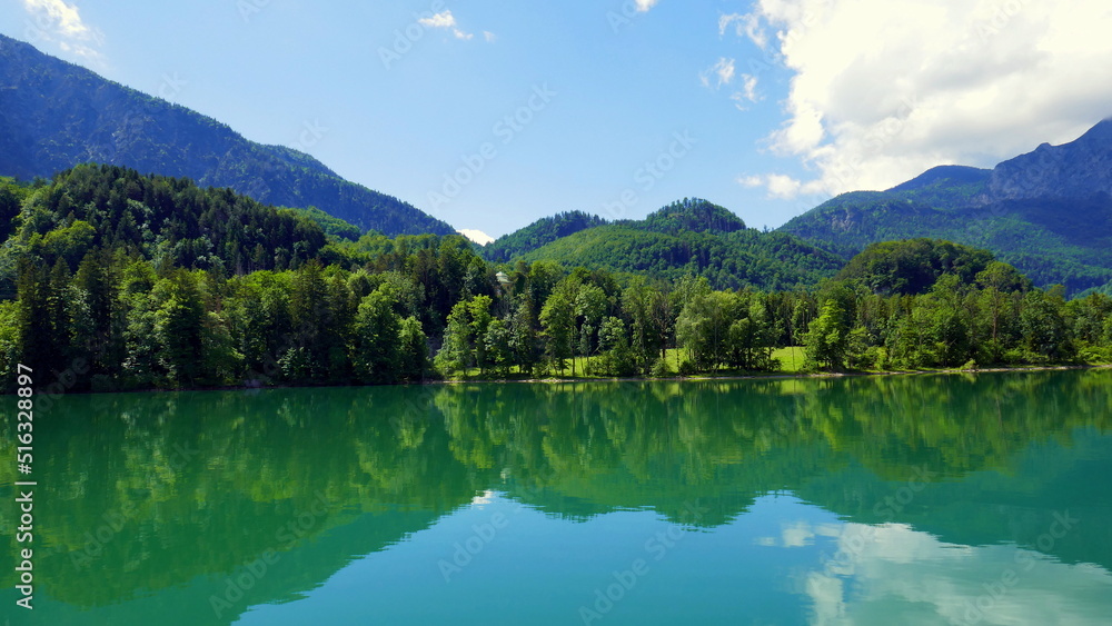 schöner Blick auf Ufer des Kochelsees in Bayern mit Badestrand, Berg, Wald, blauem Himmel und Wolken