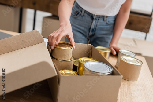 cropped view of african american woman packing canned food in box in volunteer center. © LIGHTFIELD STUDIOS