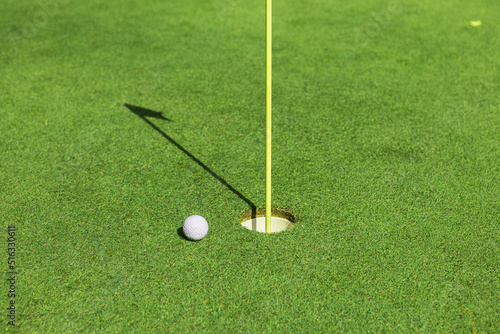 A golf ball near the hole with the flag on the golf course on the green grass