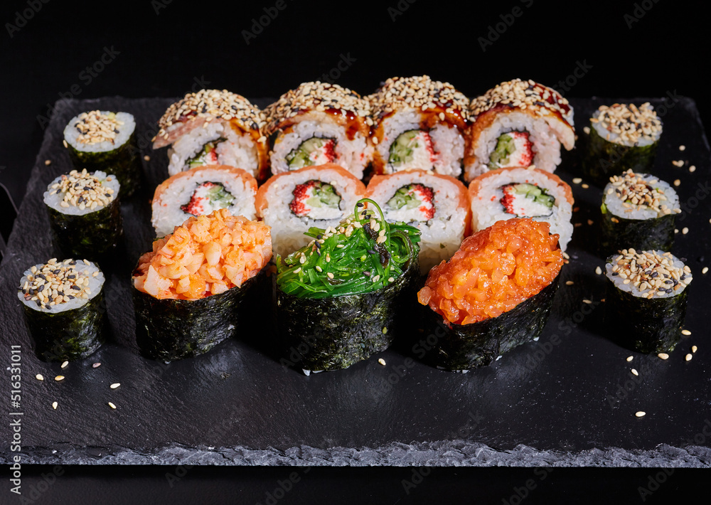 Close up of a set of sushi rolls on a black stone board on a dark table. Close up of a set of sushi rolls on a black stone board on a dark table.