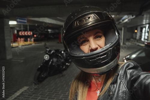 Young beautiful woman in a helmet takes a selfie in a parking garage in front of her motorcycle