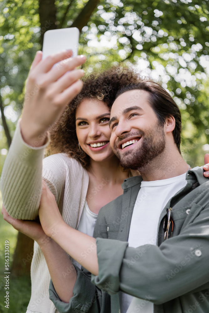 cheerful young couple taking selfie on blurred smartphone in green summer park. cheerful young couple taking selfie on blurred smartphone in green summer park.
