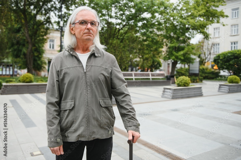 Elderly man walks with a cane in a city spring park. Elderly man walks with a cane in a city spring park.