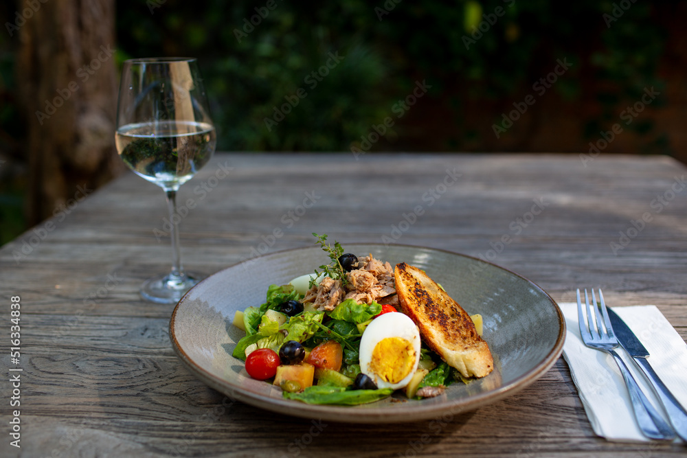 Fresh vegetable salad of tomatoes, cucumbers, italian mix, lettuce, bread, eggs and grilled chicken breast with white glass of wine. Healthy food.
