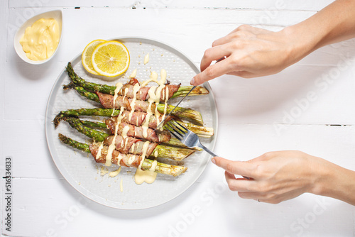 Grilled green asparagus wrapped with bacon. Female hands holds knife and fork. Ketogenic diet. Healthy food