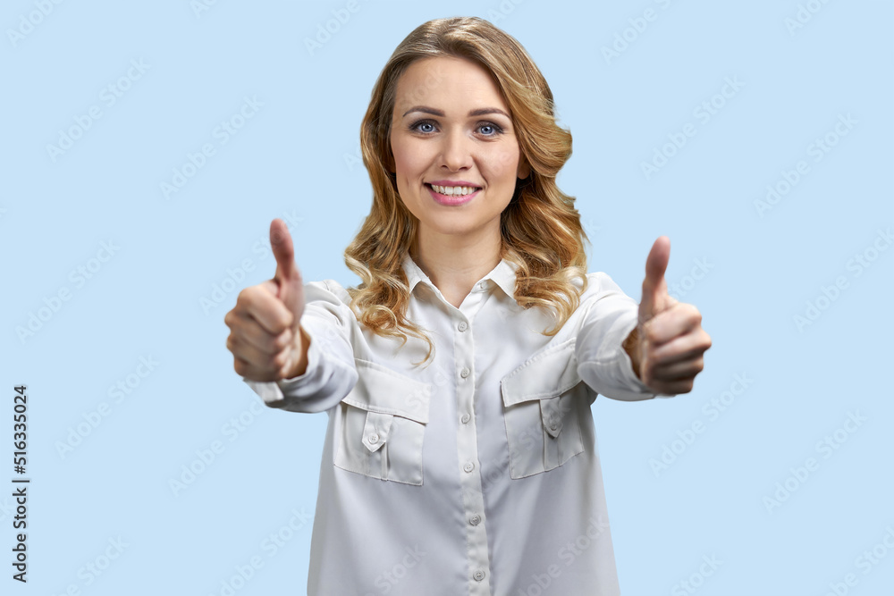 Young pretty woman in white blouse gesturing thumbs up with both hands. Woman showing thumbs up on blue background. Young pretty woman in white blouse gesturing thumbs up with both hands. Woman showing thumbs up on blue background.