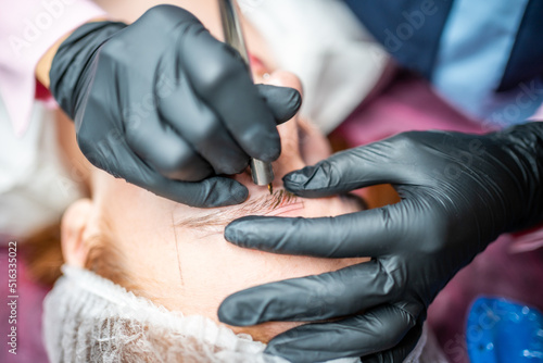 Procedure of eyebrow microblading. A master in black gloves is doing a blending needle of model s brow.