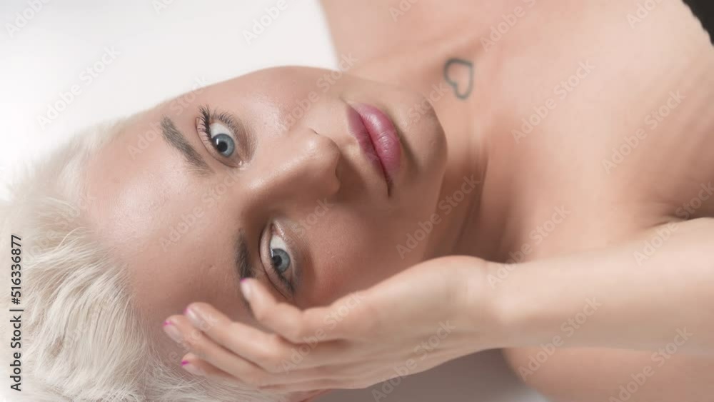 Beautiful young slim blond Caucasian woman strokes her face looking at the camera through rippling water on white background | Skin moisturizing concept Beautiful young slim blond Caucasian woman strokes her face looking at the camera through rippling water on white background | Skin moisturizing concept