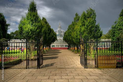 Scenic view of a glasshouse in Queen's Park in Glasgow, Scotland with green trees on a gloomy day photo