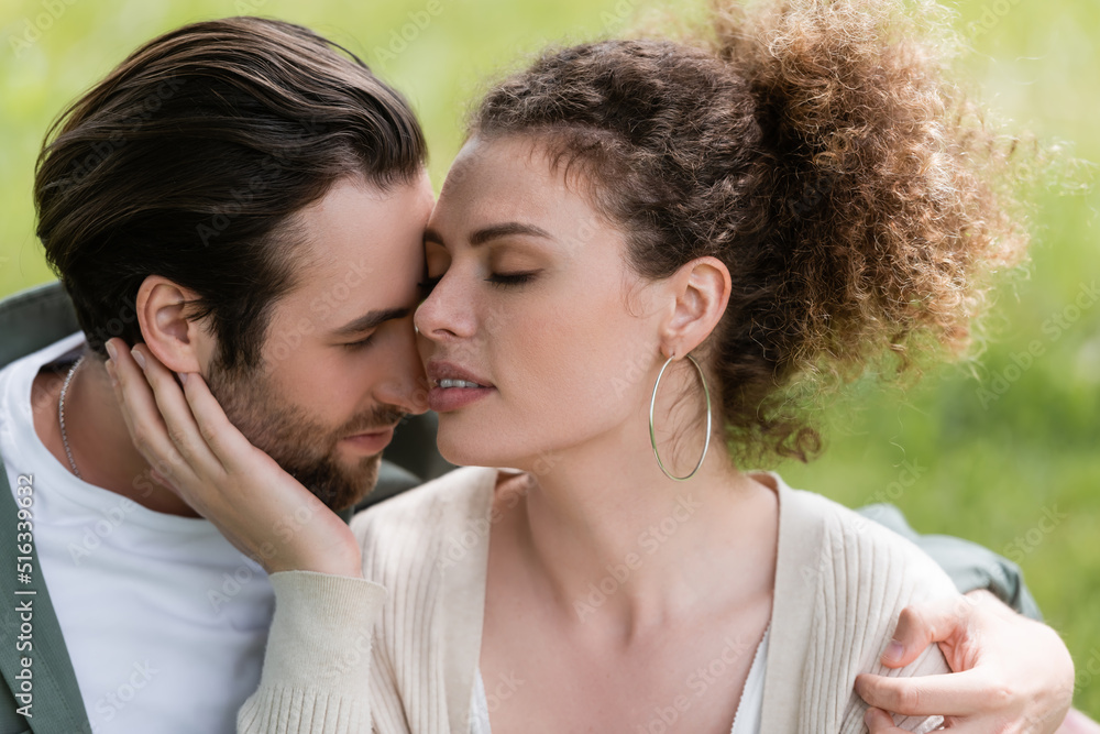 tender and curly woman touching face of bearded man in park. tender and curly woman touching face of bearded man in park.