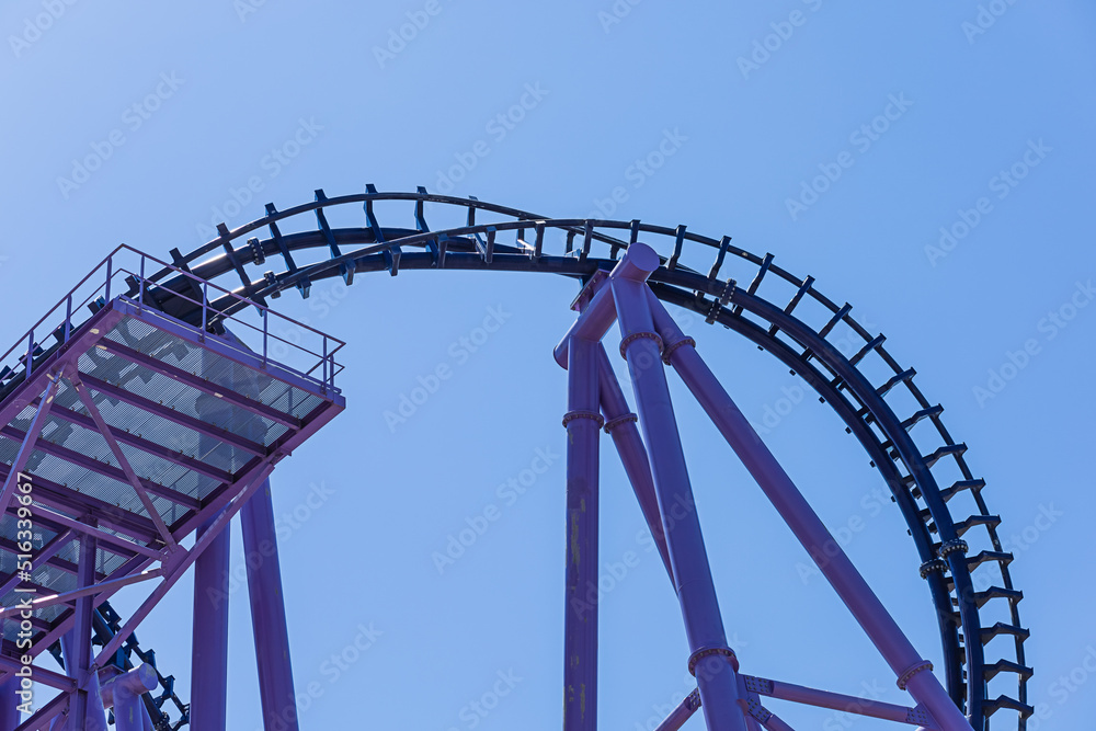 Part of a blue-purple rollercoaster against a cloudless blue sky. Extreme attraction. Metal construction.