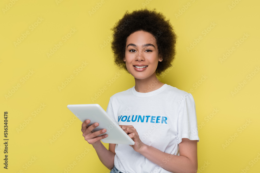african american volunteer with digital tablet smiling at camera isolated on yellow. african american volunteer with digital tablet smiling at camera isolated on yellow.