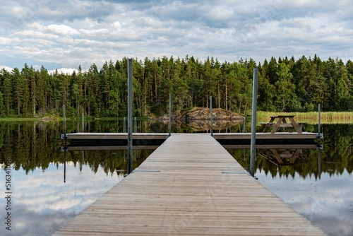 Wooden pier over a lake surrounded by trees under a blue cloudy sky photo