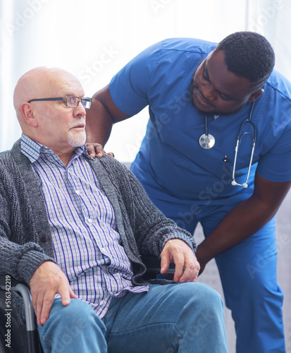 Professional doctor helps an elderly man with chronic diseases. Therapist and patient in home interior. Health care and medicine concept.