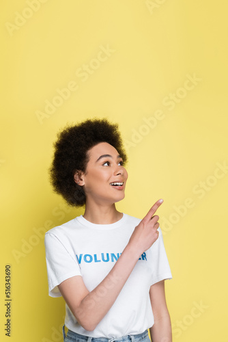 positive african american volunteer looking away while pointing with finger isolated on yellow.