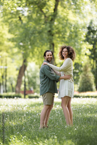 full length of joyful young couple having date in green summer park.