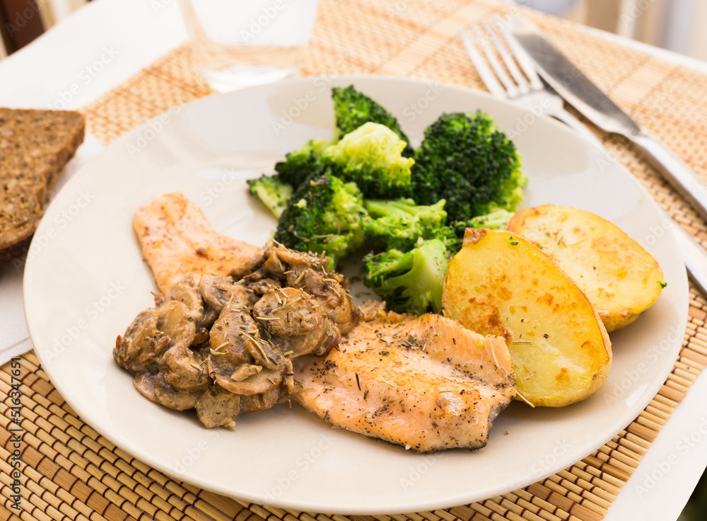 fried river trout fillet with a complex side dish of broccoli, baked potatoes and mushroom sauce