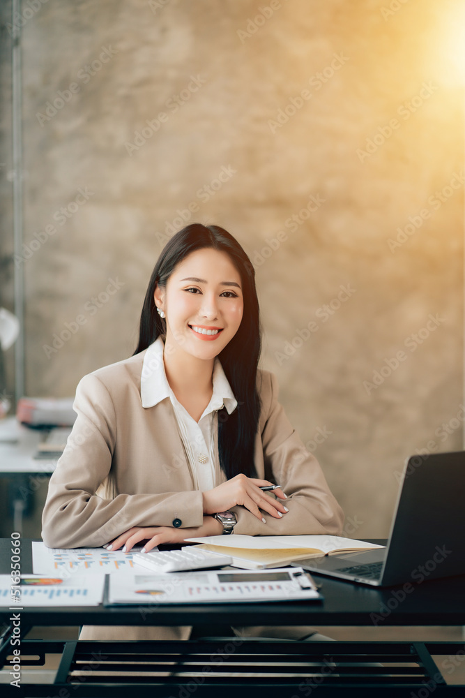 Portrait of attractive woman sitting at office desk, writing on notebook and looking at laptop screen