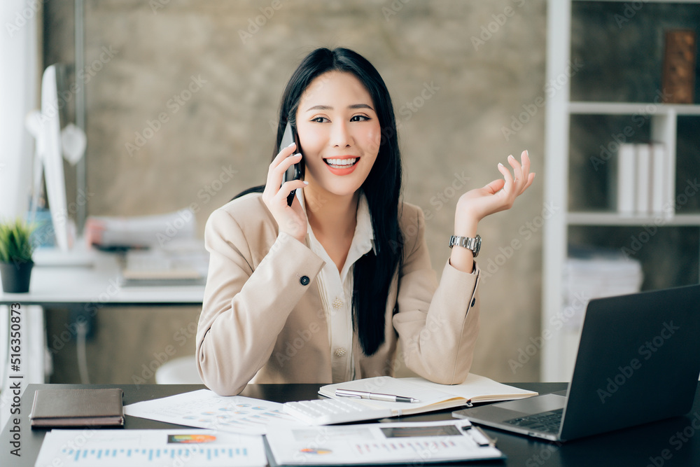 Portrait of attractive woman sitting at office desk, writing on notebook and looking at laptop screen Portrait of attractive woman sitting at office desk, writing on notebook and looking at laptop screen