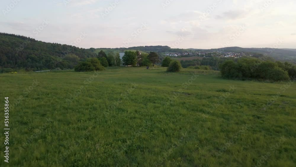 Motorcyclist standing within an expansive, lush meadow in the European countryside. Fast aerial pull away shot Motorcyclist standing within an expansive, lush meadow in the European countryside. Fast aerial pull away shot