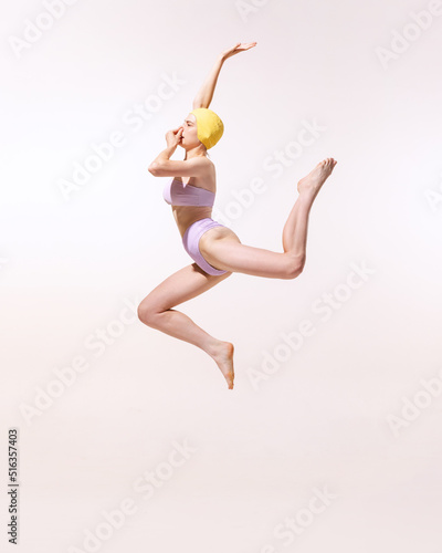 Portrait of young woman in swimming suit and cap jumping into water isolated on grey studio background. Summer activity.