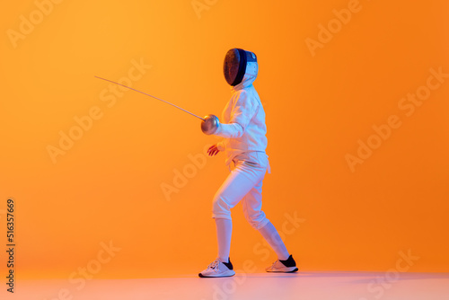 Принти на полотні Studio shot of professional fencer in white fencing costume and mask in action, motion isolated on orange color background