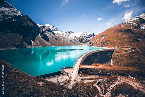 Fototapeta Scenic view of a water dam surrounded by snowy mountains on a sunny day