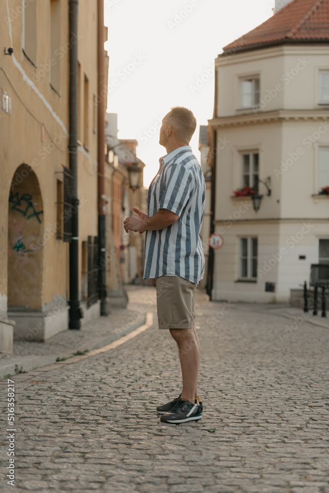 A middle-aged male tourist is looking at the sights in an old European town. A man in a shirt and shorts in Warsaw in the evening.