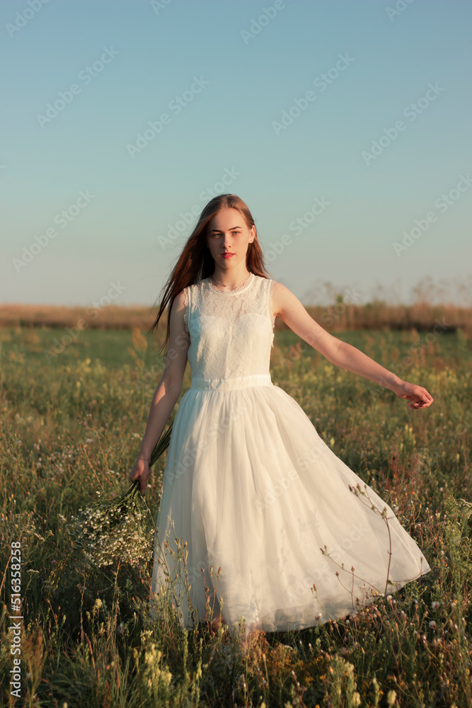 Romantic woman dancing in a wonderful flower field. Warm sunset colors