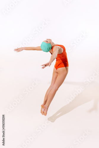 Portrait of young woman in swimming suit and cap jumping into water isolated over grey studio background. Pool diving