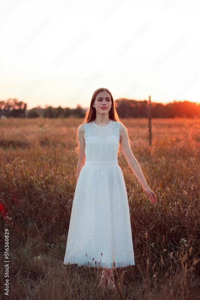 A beautiful pretty girl is dancing on a field at sunset in a white dress. Happy woman. Concept. Bride