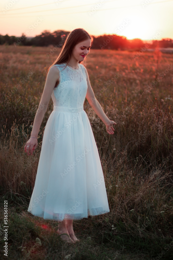 A beautiful pretty girl is dancing on a field at sunset in a white dress. Happy woman. Concept. Bride