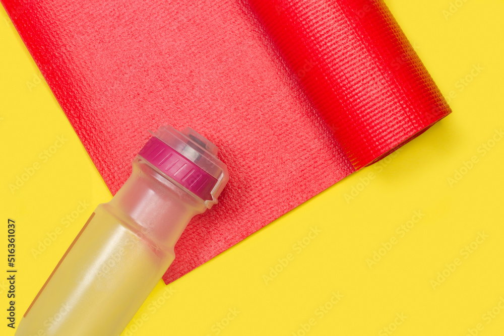 Colchoneta para yoga gimnasia roja junto a una botella de plástico sobre un fondo blanco amaillo liso y aislado. Vista superior y de cerca. Copy space. Concepto: Deportes - obrazy, fototapety, plakaty 