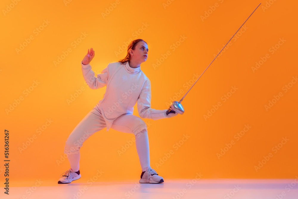 Studio shot of professional fencer in white fencing costume and mask in action, motion isolated on orange color background. Sport, youth, activity, skills,