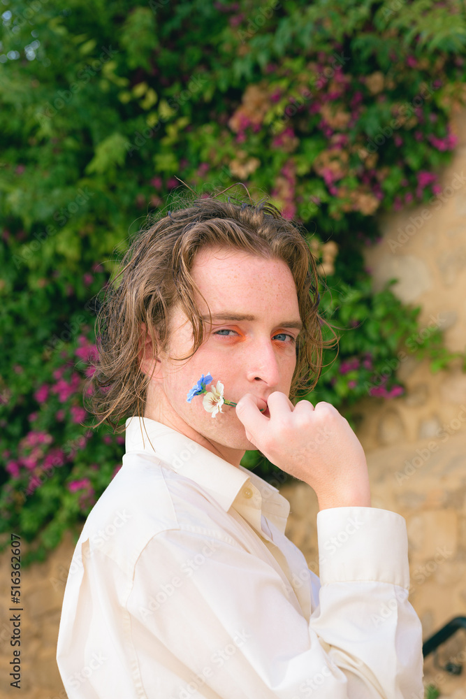 Attractive young man with make-up poses with flowers looking at camera Attractive young man with make-up poses with flowers looking at camera