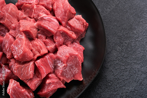 Raw chopped beef meat. Raw organic meat beef or lamb, spices, herbs on black plate on dark grey concrete background. Goulash. Raw uncooked meat. Meat with blood. Top view with copy space.