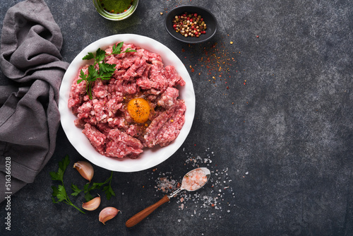 Raw minced meat. Ground meat beef, pork or lamb spices, herbs and eggs on white plate on black old concrete background. Fresh minced meat ready for cooking. Food cooking background. Top view.