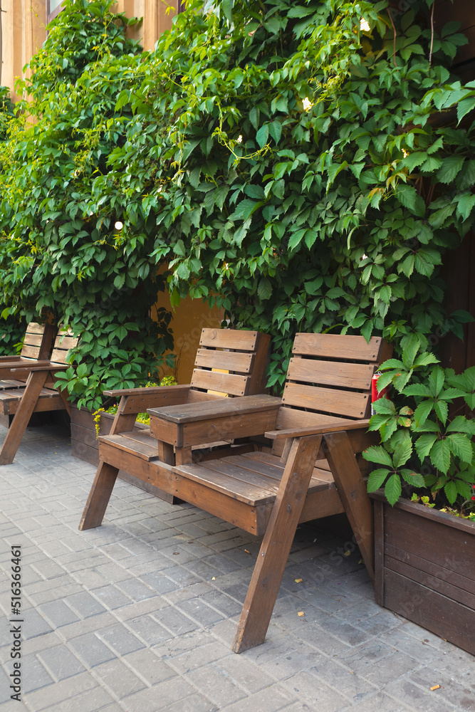 Wood bench in the bushes. Wood chairs with table in front of cafe.